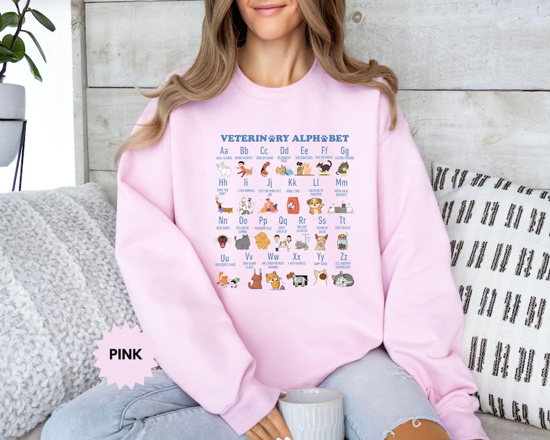 May include: A light pink sweatshirt featuring the text "VETERINARY ALPHABET" and an alphabet chart with animal illustrations. The word "PINK" is displayed in a pink banner at the bottom left.