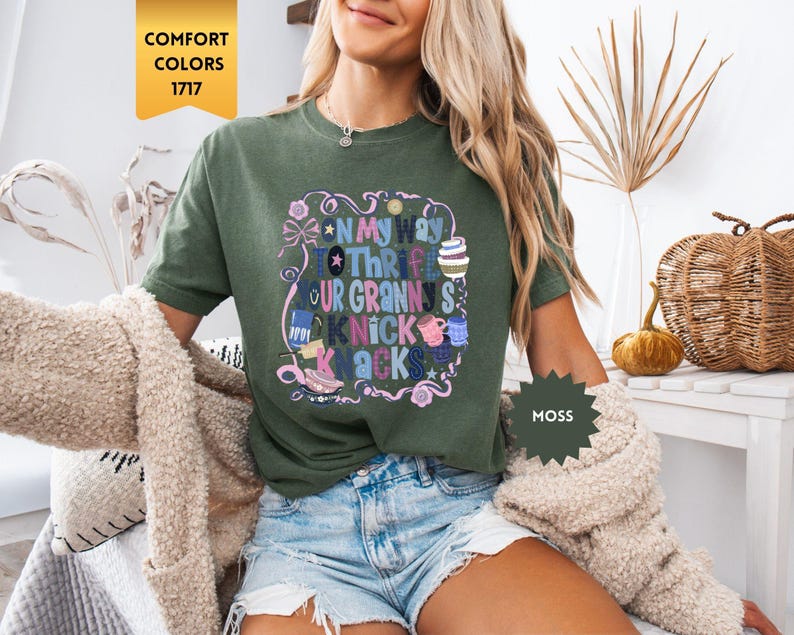 Może przedstawiać: Zielona koszulka w kolorze mchu z napisem "On My Way To Thrift Your Granny's Knick Knacks" w kolorowym, fantazyjnym wzorze. Koszulka jest w stylu Comfort Colors 1717.