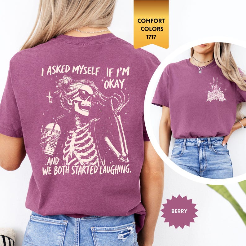 May include: Berry-coloured t-shirt featuring a skeleton graphic. The skeleton wears sunglasses and holds a drink. Text on the shirt reads, "I asked myself if I'm okay, and we both started laughing." The shirt has a crew neck and short sleeves.
