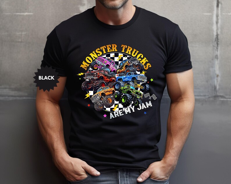 May include: Black t-shirt featuring a colorful graphic of monster trucks. The design includes the text "MONSTER TRUCKS ARE MY JAM" in yellow and white, with a checkered flag and lightning bolt accents. The shirt is black.