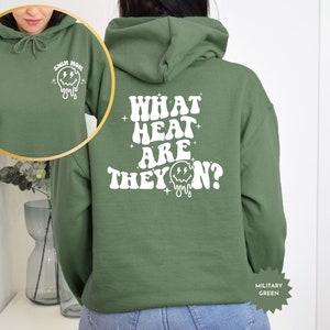 May include: Green hooded sweatshirt with the text "WHAT HEAT ARE THEY ON?" in white with a dripping smiley face graphic. The sweatshirt has a small white smiley face graphic on the left sleeve with the text "SWIM MOM".