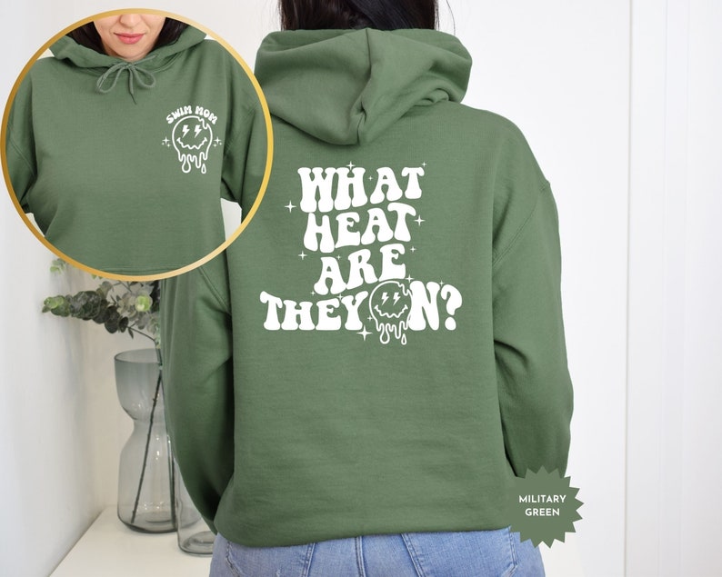 May include: Green hooded sweatshirt with the text "WHAT HEAT ARE THEY ON?" in white with a dripping smiley face graphic. The sweatshirt has a small white smiley face graphic on the left sleeve with the text "SWIM MOM".