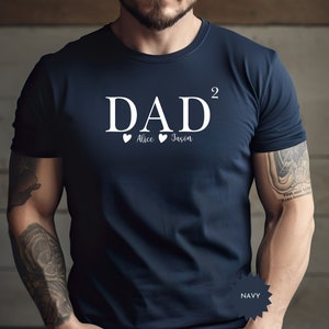 May include: Navy blue t-shirt with the word "DAD²" in white, with "Alice" and "Jason" below, each with a heart symbol. The shirt is a crew neck style.
