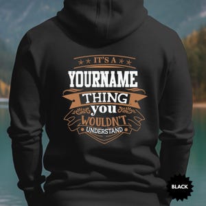 May include: Black hoodie featuring the text "YOURNAME THING YOU WOULDN'T UNDERSTAND" in white and brown. The hoodie has a hood and a drawstring. The word "BLACK" is printed on the bottom right corner.
