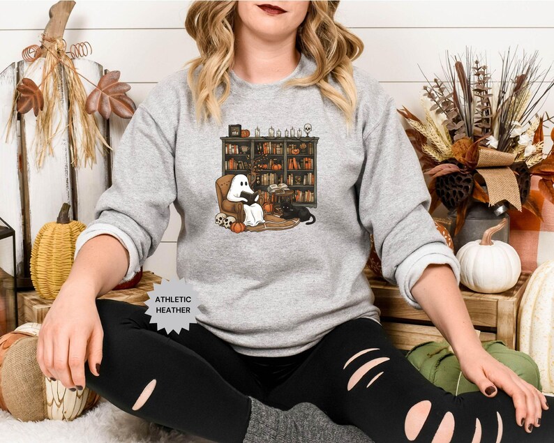 May include: A gray sweatshirt with a ghost reading a book in a library setting. The ghost is white and has a black cat sitting next to it. The text "Athletic Heather" is on the bottom of the sweatshirt.