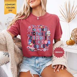 Może przedstawiać: Koszulka w kolorze karmazynowym z napisem "ON MY WAY TO THRFT YOUR GRANNY'S NICK KNACKS" w kolorowym, fantazyjnym wzorze. Koszulka jest w stylu Comfort Colors 1717.