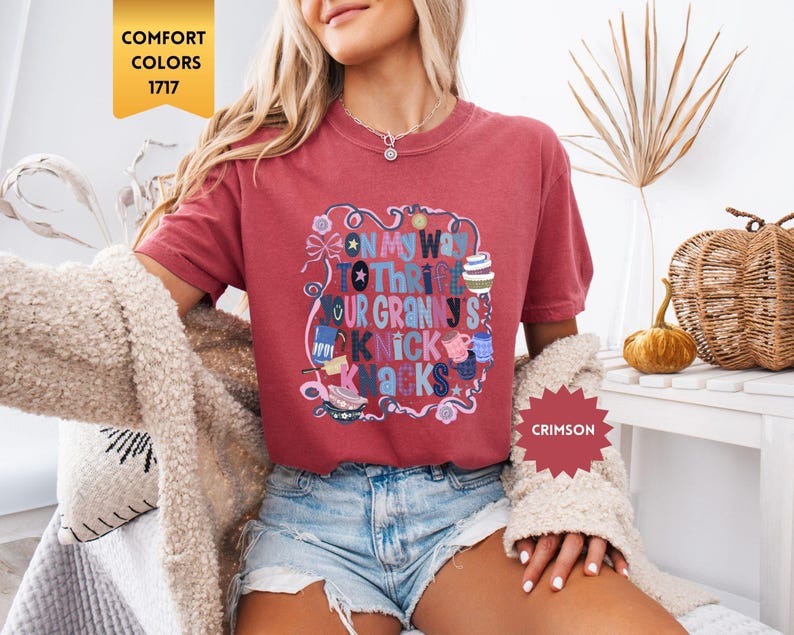 Może przedstawiać: Koszulka w kolorze karmazynowym z napisem "ON MY WAY TO THRFT YOUR GRANNY'S NICK KNACKS" w kolorowym, fantazyjnym wzorze. Koszulka jest w stylu Comfort Colors 1717.