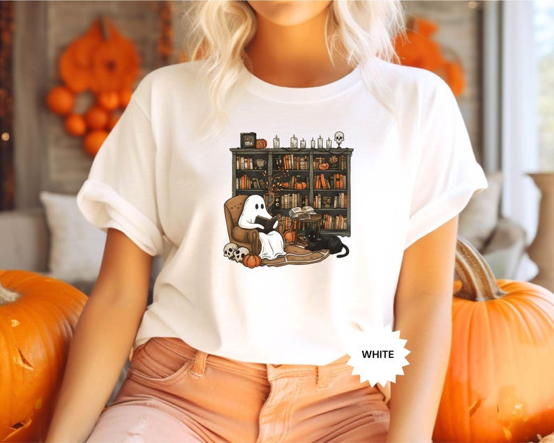 May include: White t-shirt with a graphic of a ghost reading a book in a library with a black cat. The text "WHITE" is visible in the bottom right corner of the image.