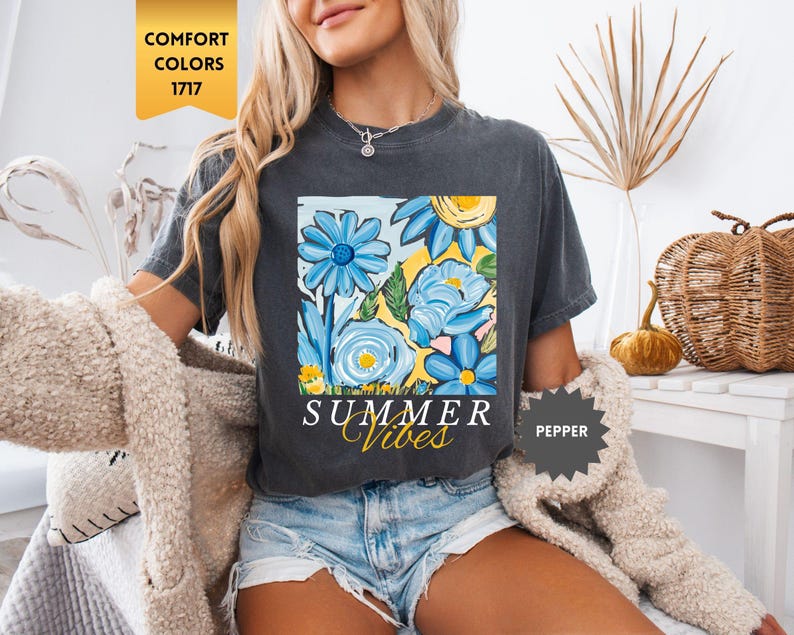 Peut inclure: Un t-shirt gris fonc&eacute; avec un motif de fleurs color&eacute;es et le texte "Summer Vibes" imprim&eacute; sur le devant. Le t-shirt a des manches courtes et un col rond.
