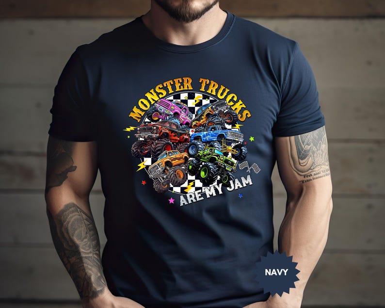 May include: Navy blue t-shirt featuring a colorful graphic of monster trucks. The design includes the text "MONSTER TRUCKS ARE MY JAM" in a circular arrangement. The shirt is a solid navy color.