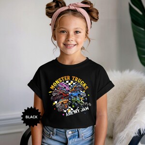 May include: Black t-shirt featuring a colorful graphic of monster trucks. The design includes the text "MONSTER TRUCKS ARE MY JAM" in a circular arrangement. The shirt is worn by a young person.