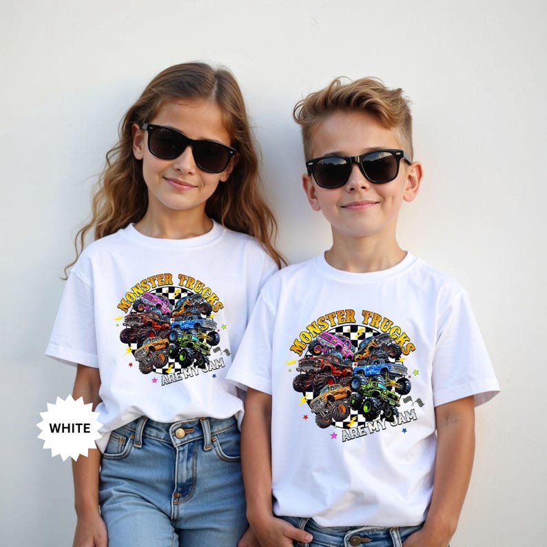 May include: Two children wearing white t-shirts with a colorful monster truck graphic. The graphic features various monster trucks arranged around a checkered circle with the text "Monster Trucks Are My Jam". The shirts are paired with blue jeans.