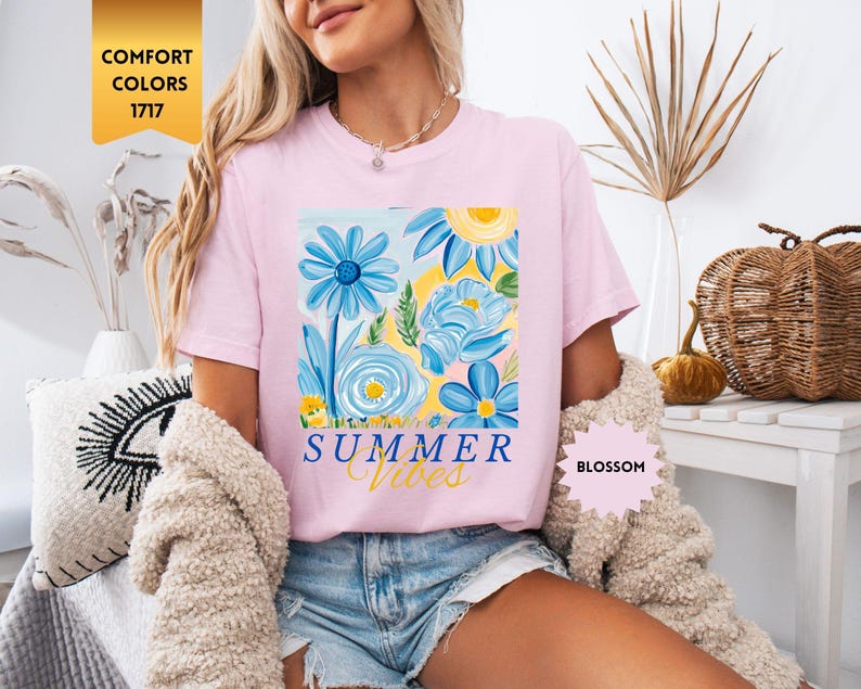 Peut inclure: T-shirt rose avec un motif floral et le texte "Summer Vibes" imprim&eacute; sur le devant. Le motif floral pr&eacute;sente des fleurs bleues, jaunes et roses.