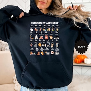 May include: Black hooded sweatshirt featuring the text "VETERINARY ALPHABET" with an illustrated alphabet of dog breeds. The sweatshirt has a front pocket and a black starburst tag that says "BLACK".