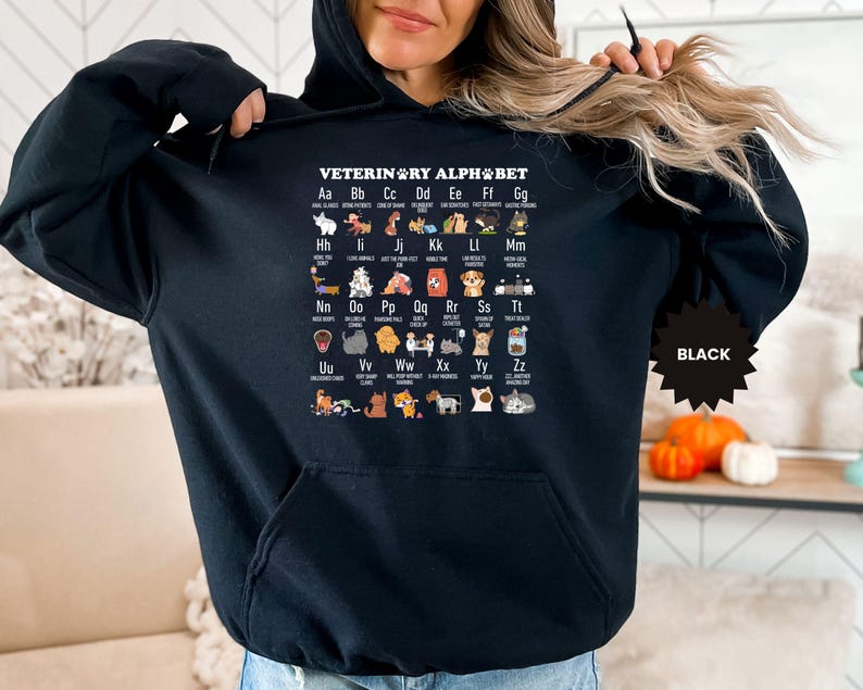 May include: Black hooded sweatshirt featuring the text "VETERINARY ALPHABET" with an illustrated alphabet of dog breeds. The sweatshirt has a front pocket and a black starburst tag that says "BLACK".