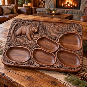 May include: A rectangular brown wooden serving tray featuring a carved relief of a bear in a forest landscape with mountains. The tray includes five smooth, recessed oval compartments for food, surrounded by detailed carvings of pine cones and oak leaves.