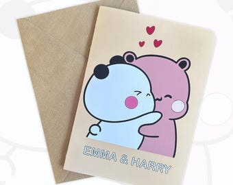 May include: A greeting card with a light beige background featuring a cartoon illustration of a light blue bear and a pink bear hugging. Three small red hearts are above them. The text EMMA & HARRY is printed in blue below the bears. A brown envelope is included.