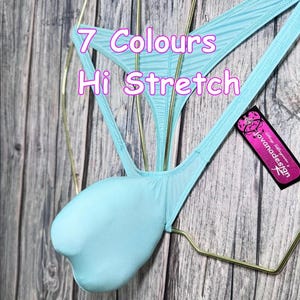 May include: Light blue thong-style underwear with a pouch. The text "7 Colours Hi Stretch" is visible. A tag with the brand name "Jovanadesign" is attached. The garment is displayed on a gold-colored hanger.