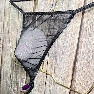 May include: Black mesh lingerie with a satin trim. The lingerie is hanging on a gold metal hanger.