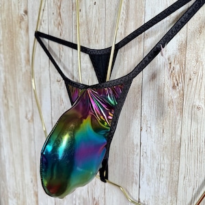 Puede incluir: Una tanga con una bolsa metálica e iridiscente que cambia entre tonos verdes, azules, morados y dorados. La prenda está confeccionada con tiras elásticas finas de color negro y ribetes negros, mostrando un acabado brillante y reflectante en toda la zona frontal.