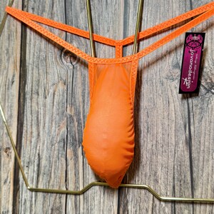 Op de afbeelding: Oranje mesh string ondergoed hangend aan een gouden hanger. Het ondergoed heeft een jovanadesign-label.