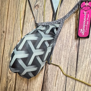 Könnte beinhalten: Schwarze und graue gemusterte Dessous mit schwarzem Satinbesatz. Die Dessous hängen an einem goldenen Kleiderbügel mit einem Etikett mit der Aufschrift "javamadesign".