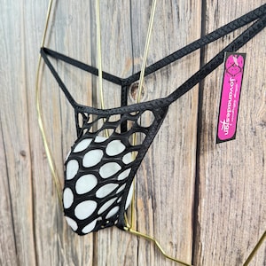 May include: Black mesh thong underwear with a white polka dot pouch. The underwear is displayed on a gold hanger against a wooden background. A pink tag with the text "jovanadesign" is attached.