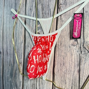 May include: Red and white Christmas-themed thong underwear with "HO HO HO" text and snowflake patterns. The underwear has a white trim and a tag with the brand name "jovanadesign".