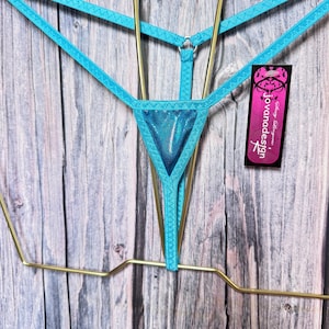 May include: A bright turquoise thong featuring a metallic triangular front panel, thin elastic straps, and a central metal ring connector. A black rectangular tag attached to the side displays the text jovanadesign in white lettering.