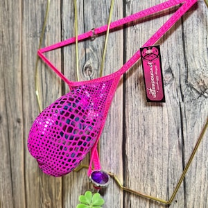 May include: A hot pink bikini bottom with a textured, scale-like pattern. The bikini bottom has a small, decorative purple gem and a green four-leaf clover charm. The tag reads "Javanadesign".
