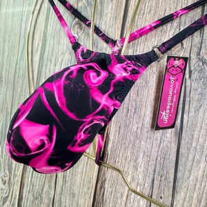 May include: Pink and black patterned underwear with a Jovani Design tag. The underwear has a low rise cut and is made of a stretchy fabric.