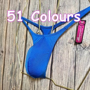 Puede incluir: Un tanga de traje de baño azul vibrante exhibido en una percha dorada. El texto "51 Colores" es visible en rosa. Una etiqueta con la marca "jovanadesign" está adjunta.