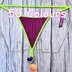 May include: A dark purple thong with bright lime green trim and a small tag reading "sanadesign". The text "50 Colours" is overlaid in white with a pink outline. A purple circular charm and a peach-shaped charm hang from the bottom center.