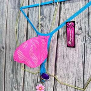 May include: A neon pink thong with a mesh front panel and blue trim is displayed on a gold wire hanger. The thong features a decorative purple gem and a pink flower charm. A tag with the text "jovanadesign" is attached.