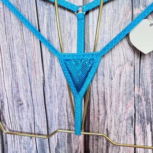 May include: A bright blue thong featuring a triangular front panel with a shimmering, glittery texture. The garment is constructed with thin, elasticized straps that connect to a central metal ring, creating a geometric, strappy design.