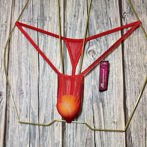 Può includere: Perizoma in rete rossa con tasca, esposto su una gruccia color oro su sfondo di legno. La biancheria intima ha un design delicato e trasparente. È attaccata una piccola etichetta con testo.