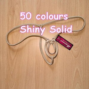 Puede incluir: Un collar gargantilla de cuero beige con un delicado diseño de múltiples bucles. El collar está etiquetado como "50 colores Shiny Solid" y "Jovanadesign".