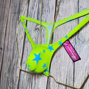 Może przedstawiać: Neonowa zielona bielizna z niebieskim wzorem w gwiazdy. Bielizna jest prezentowana na złotym metalowym wieszaku. Do bielizny dołączona jest metka z napisem "jovanadesign".