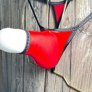 May include: Red and black lingerie with a lace trim. The lingerie is hanging on a gold hanger.