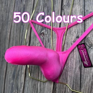 May include: Bright pink thong underwear with a pouch, displayed on a gold-colored wire hanger. The text "50 Colours" is visible in the image. A small tag with the brand name "Jovanadesign" is attached.