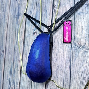 May include: A blue metallic thong swimsuit with black straps. The swimsuit is displayed on a gold wire hanger against a wooden background. A tag with the text "jovanadesign" is attached to the strap.