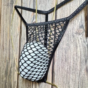 May include: Black mesh underwear with a diamond pattern. The underwear is hanging on a gold hanger against a wooden background.