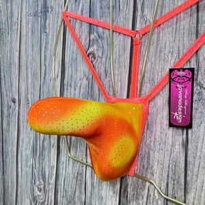 May include: A neon orange and yellow thong-style lingerie piece with a dotted pattern. The garment is suspended by a gold-colored wire frame and features a neon pink strap design. A small tag with text is attached.