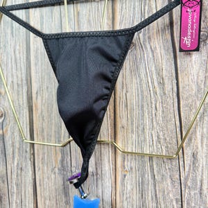 May include: Black lingerie with a star-shaped metal accent. The lingerie is hanging on a gold hanger and has a tag that reads "Jovanadesign".