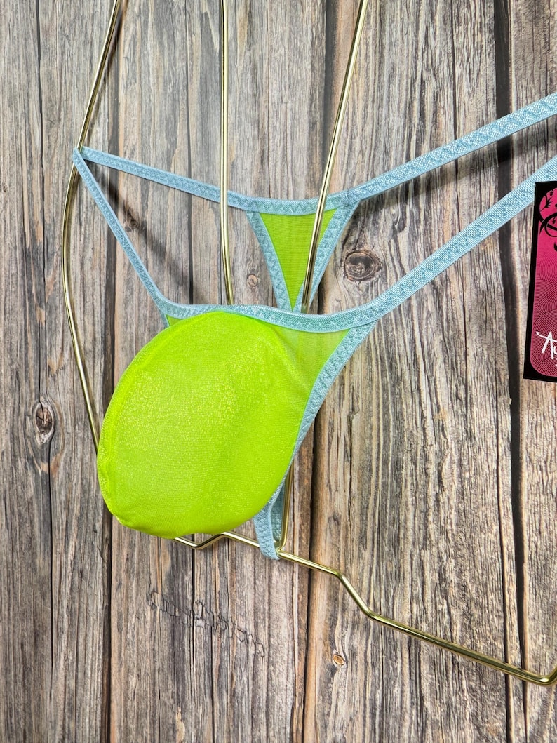 May include: Light blue mesh underwear with a lime green pouch. The underwear is hanging on a gold hanger against a wood background.