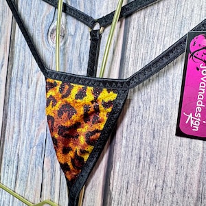 May include: A thong with a leopard print design in shades of yellow, orange, and brown, trimmed with black fabric. The straps are black and attached to a gold-colored metal ring. A pink and white tag is visible.