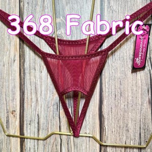 Pode incluir: Um fio dental de malha transparente vermelho escuro com um painel frontal triangular e alças elásticas finas. A peça possui uma etiqueta preta com o texto "jovanadesign" e o texto "368 Fabric" é visível na parte superior.