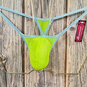 May include: Light blue and lime green mesh underwear with a tag that says "Jovanadesign" hanging on a gold metal hanger against a wood background.