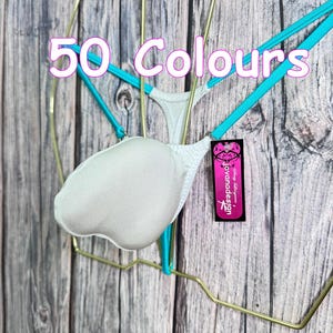 May include: White lingerie with turquoise straps and a padded front. The text "50 Colours" is displayed above the lingerie. A tag with the text "Jovanadesign" is attached to the lingerie. The lingerie is hanging on a gold wire hanger against a wooden background.