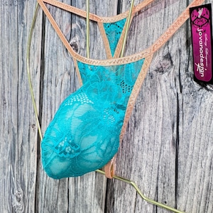 May include: A teal lace thong with peach trim, displayed on a gold hanger. The thong features a floral lace pattern and a delicate design. A tag with the text "Jovanadesign" is visible.